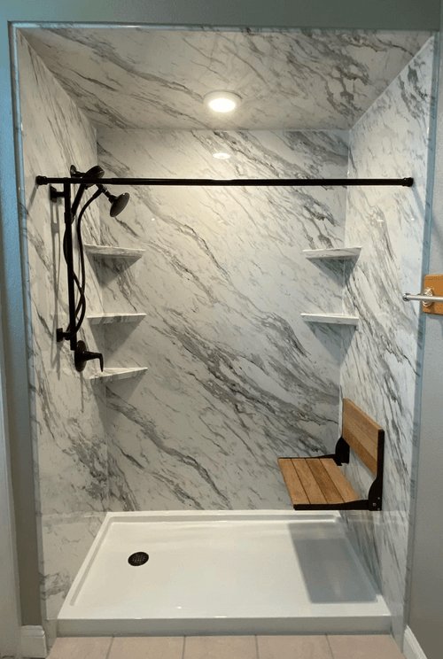 Carrara marble walk-in shower with fold-down teak bench and matte black fixtures