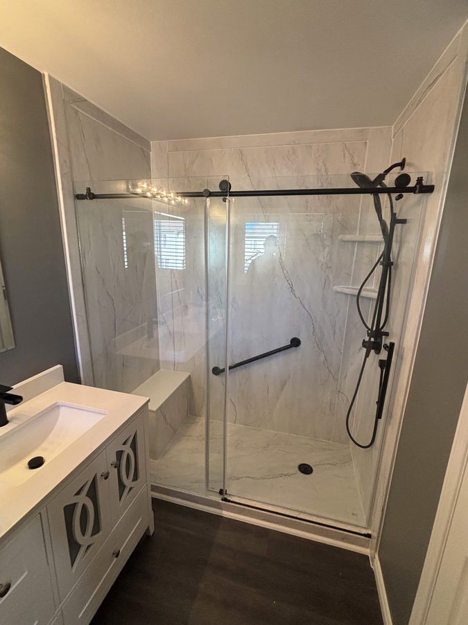 Walk-in shower with built-in corner bench, matte black fixtures, and marble-look walls