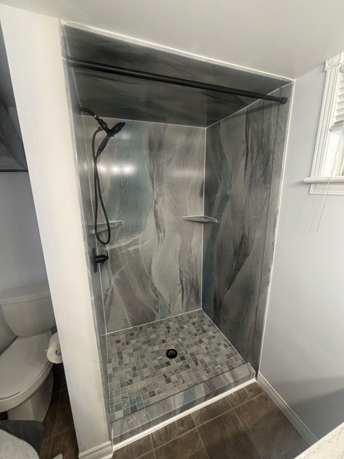 Walk-in shower stall with dramatic grey marble walls and glass mosaic floor