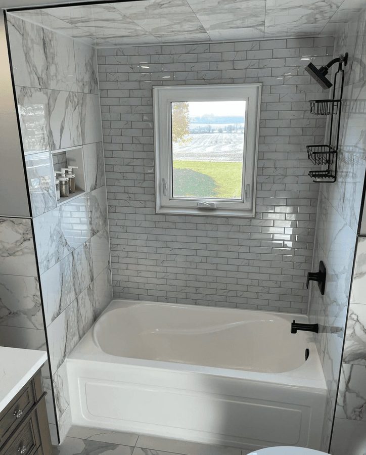 Tub-shower combo with subway and marble mix, window view, and matte black fixtures