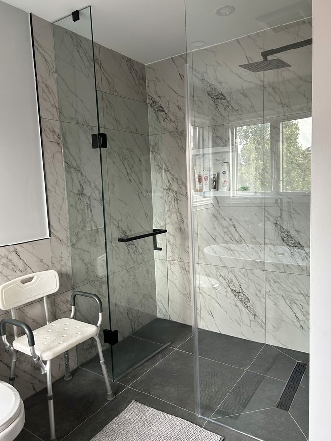 Curbless walk-in shower with shower chair, Calacatta marble walls, matte black fixtures, and linear drain